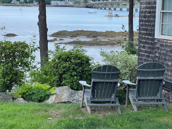 Deux fauteuils Adirondack sont placés face à un plan d’eau, avec un pont en arrière-plan.