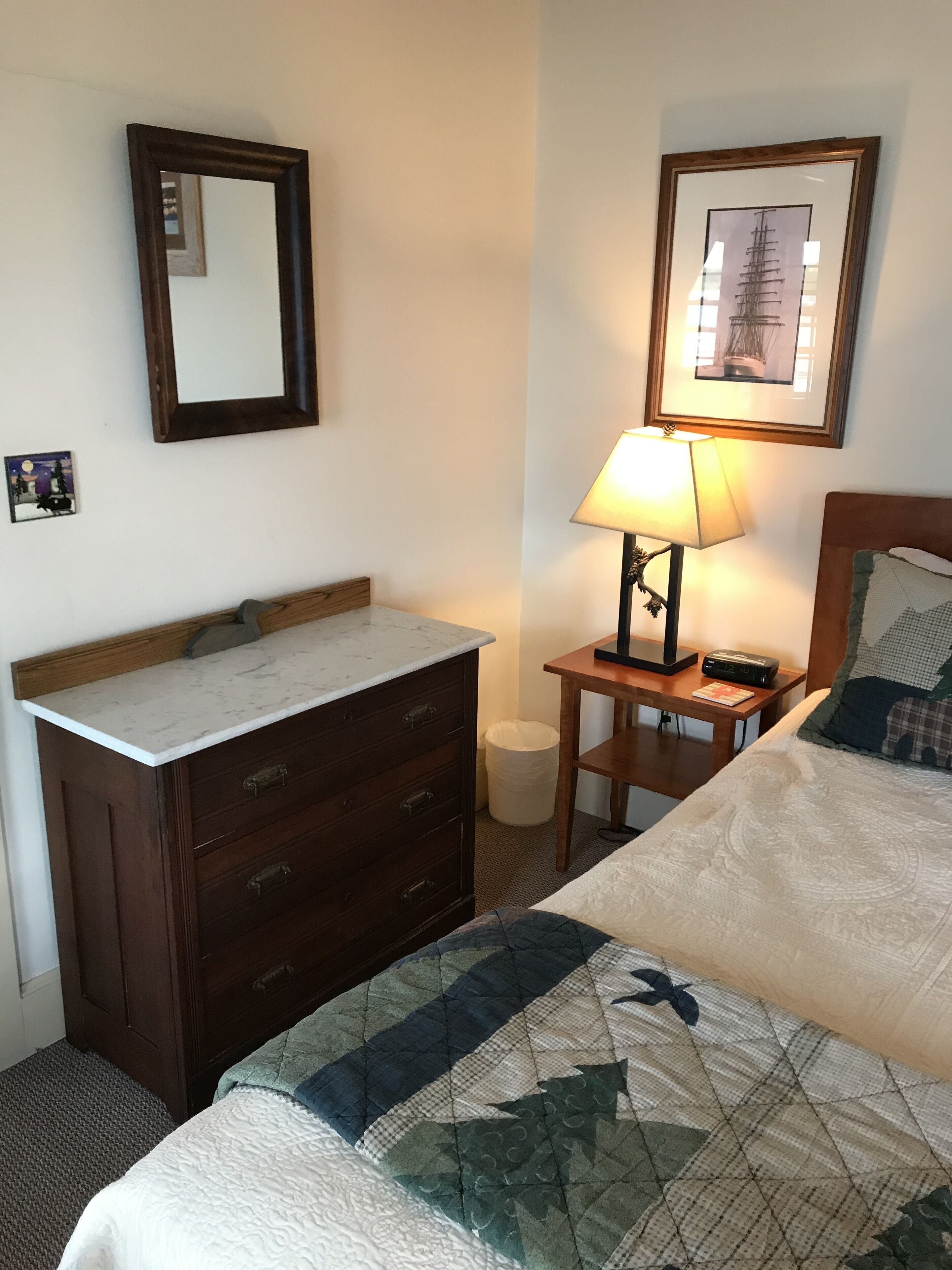 Een hotelkamer met een bed, nachtkastje met lamp, dressoir en een ingelijste foto aan de muur.