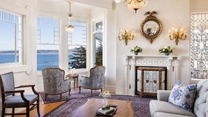 A spacious room with a large window overlooking the sea, a fireplace, and elegant furniture. - Seven Gables Inn on Monterey Bay, A Kirkwood Collection Property (Pacific Grove)