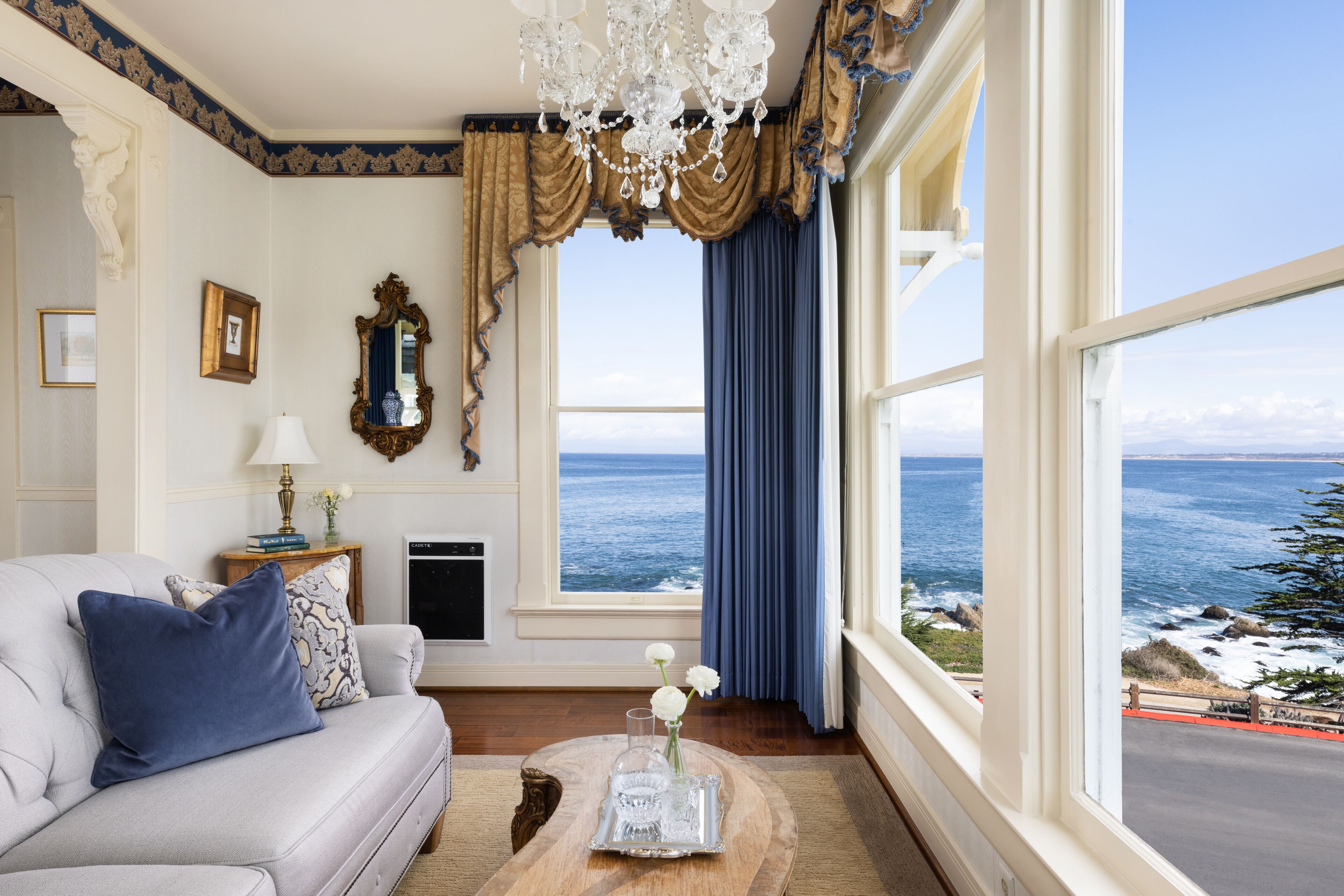 A room with a view of the ocean, a chandelier, and a sofa with decorative pillows.