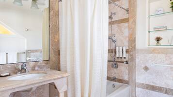 A bathroom with a bathtub, a shower, a sink, and a glass shelf with toiletries.
