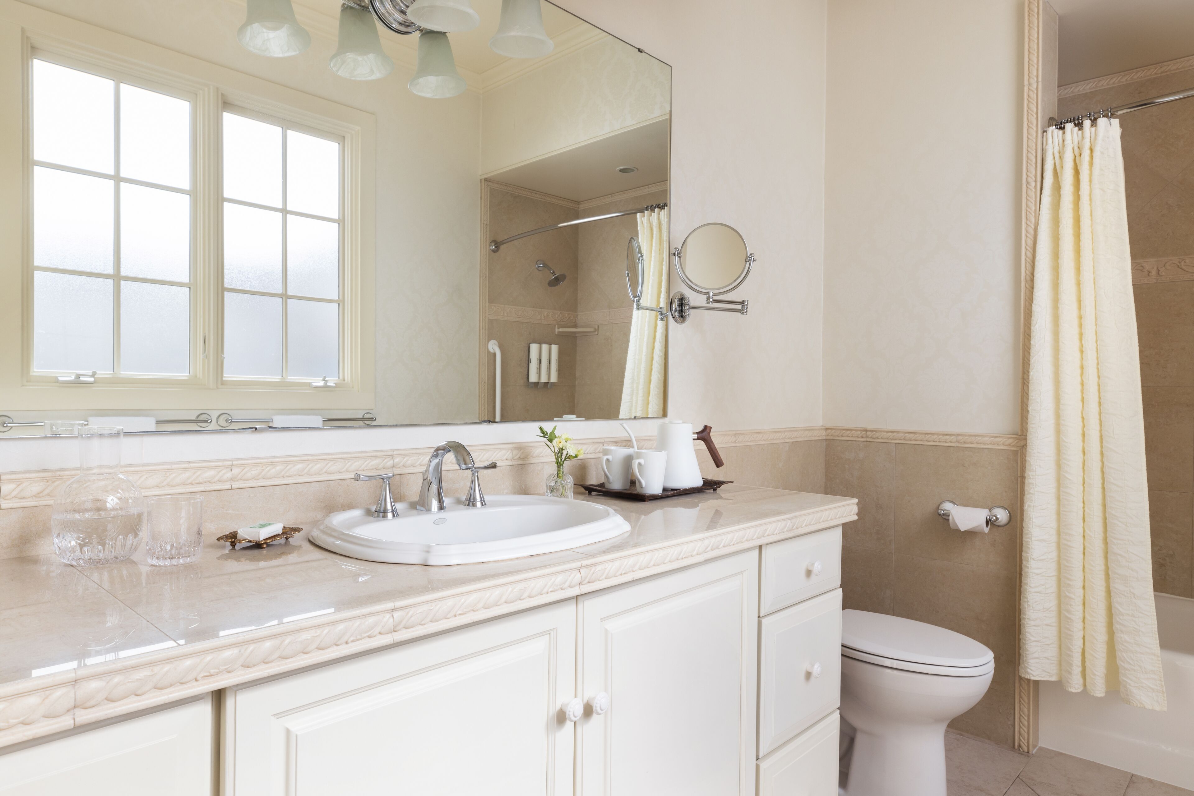 A bathroom with a white sink, mirror, and toilet. There is a window above the sink, and a shower curtain is visible.