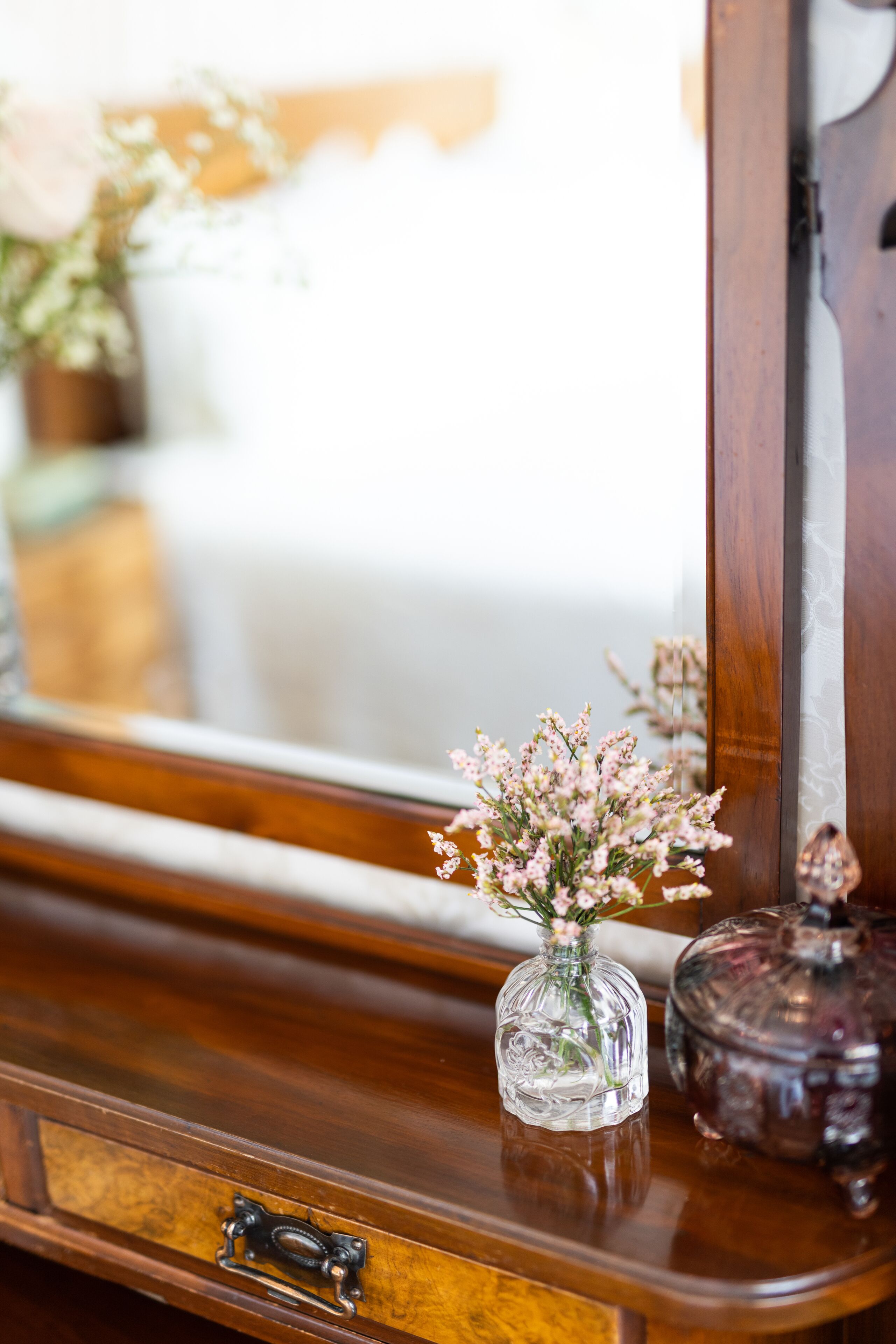 A wooden dresser with a mirror, a glass vase with flowers, and a decorative item.