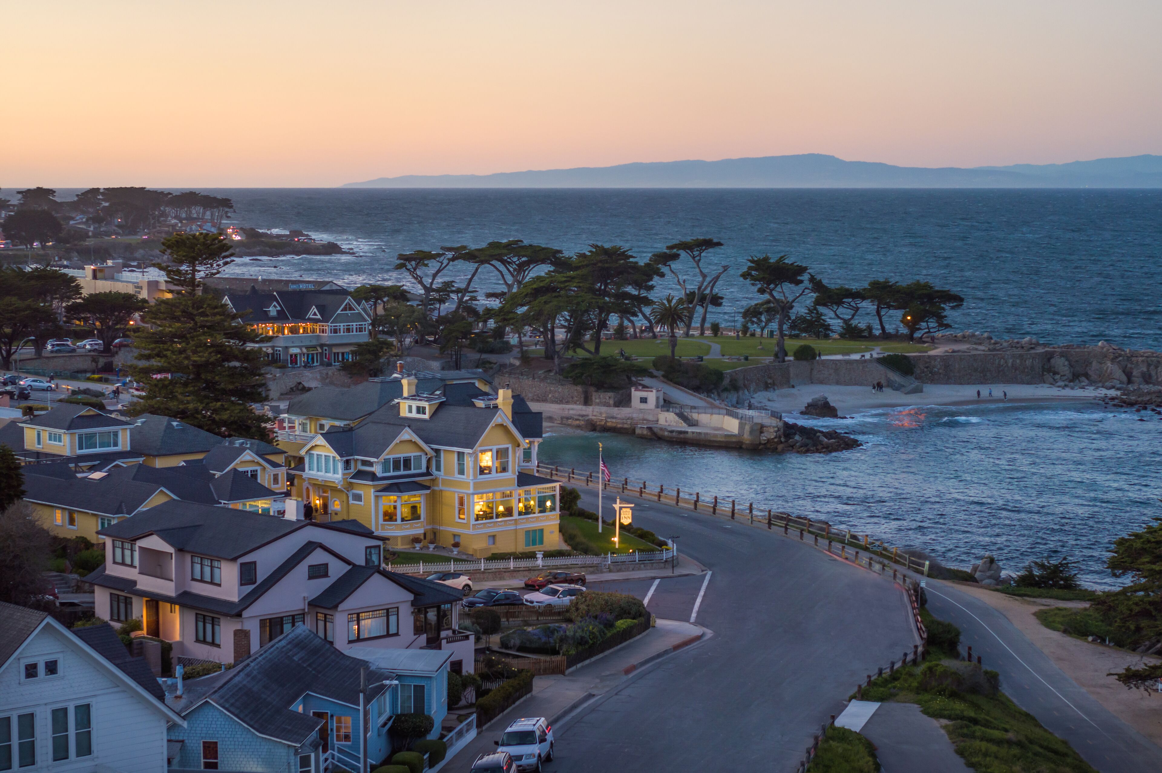 A coastal town with a prominent yellow building, a marina, and a road curving along the water.