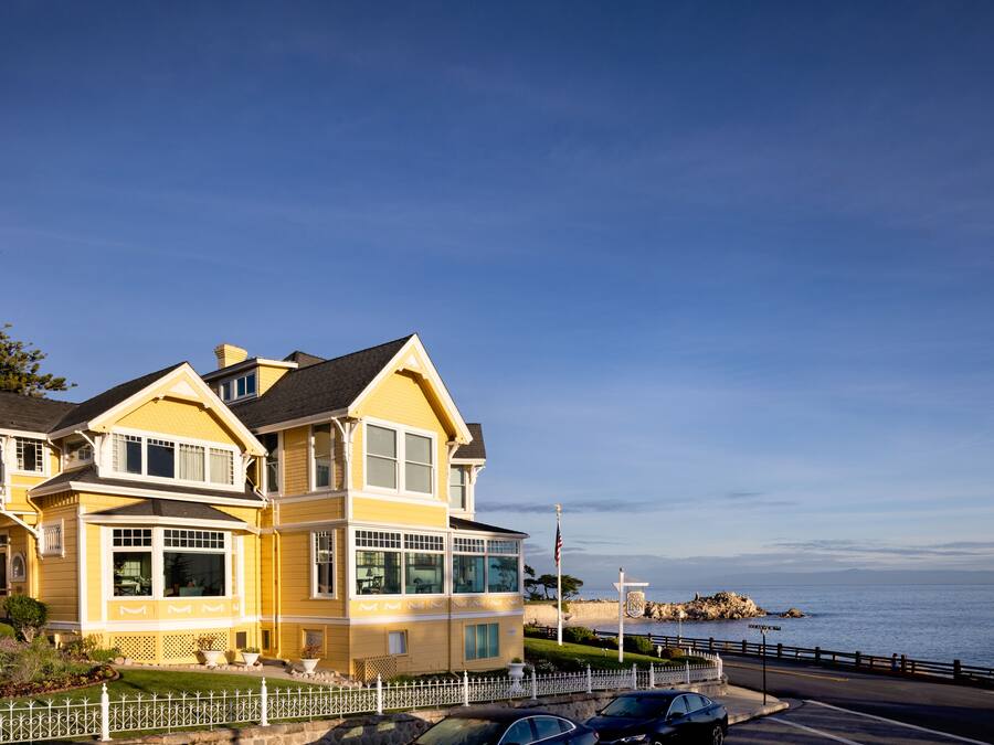 A two-story yellow house with a balcony, a garage, and a driveway with cars parked in front.