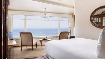 Habitación de hotel con una cama grande, dos sillones, una mesita y vista al océano.