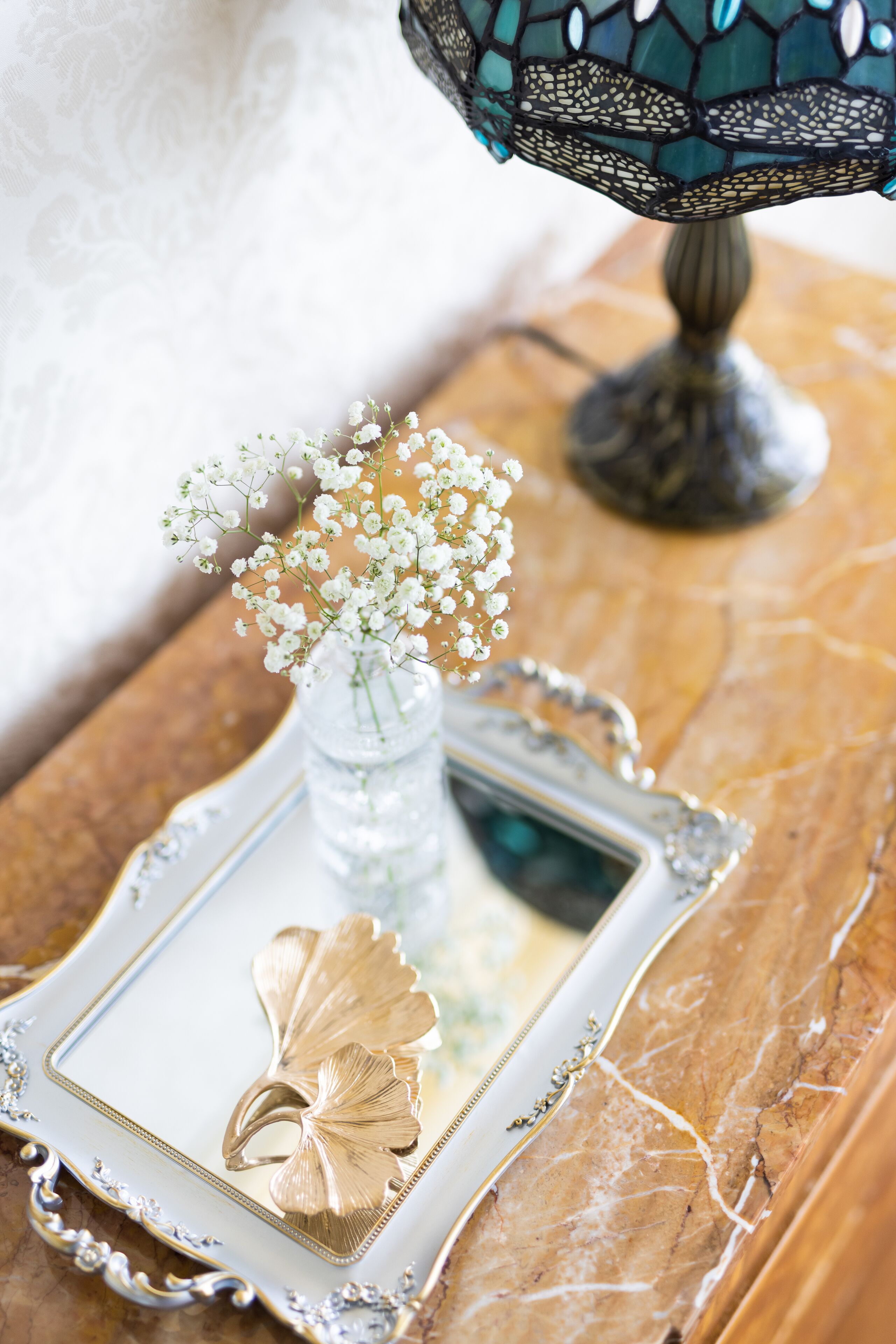 A decorative tray with a vase of flowers and a gold leaf, placed on a marble surface.