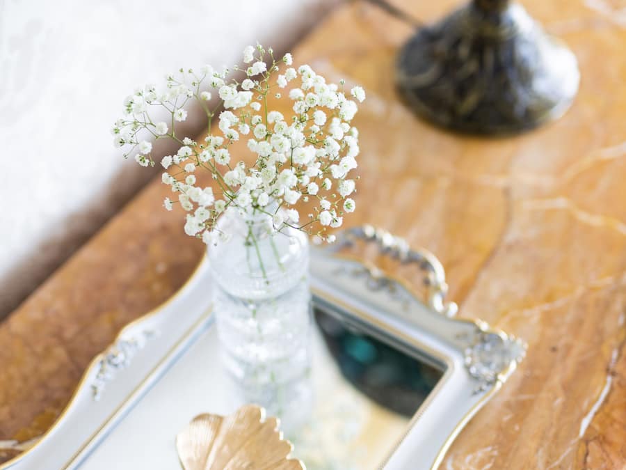 A decorative tray with a vase of flowers and a gold leaf, placed on a marble surface.