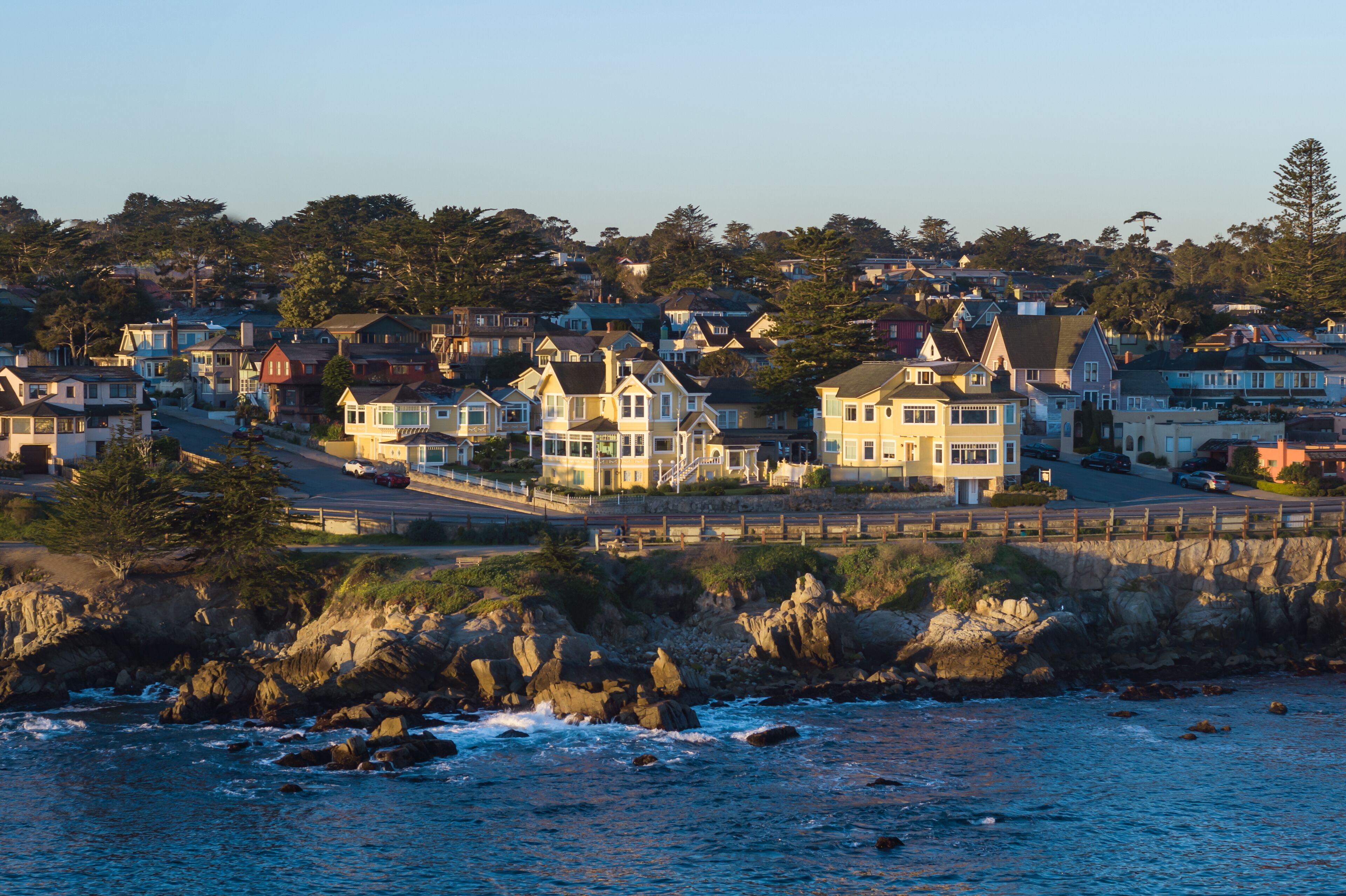 A coastal residential area with houses along the shoreline, a rocky beach, and a clear view of the ocean.