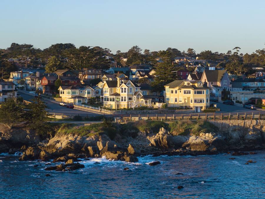 A coastal residential area with houses along the shoreline, a rocky beach, and a clear view of the ocean.