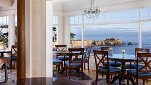 A dining area with a view of the sea, featuring a chandelier, wooden chairs, and a round table. - Seven Gables Inn on Monterey Bay, A Kirkwood Collection Property (Pacific Grove)