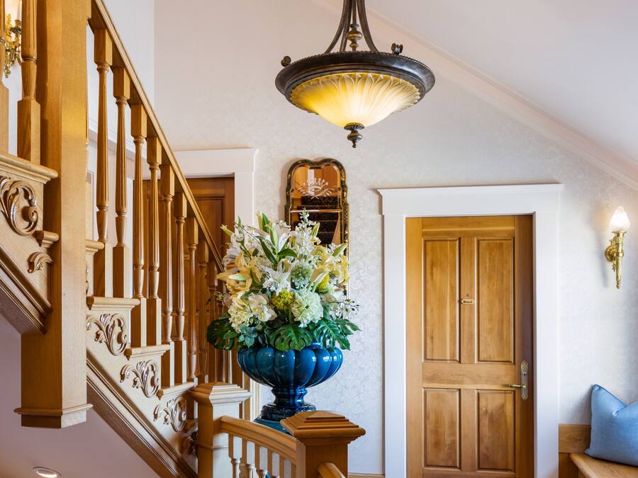 A wooden staircase with a blue vase of flowers, a patterned rug, and a wooden door at the top.