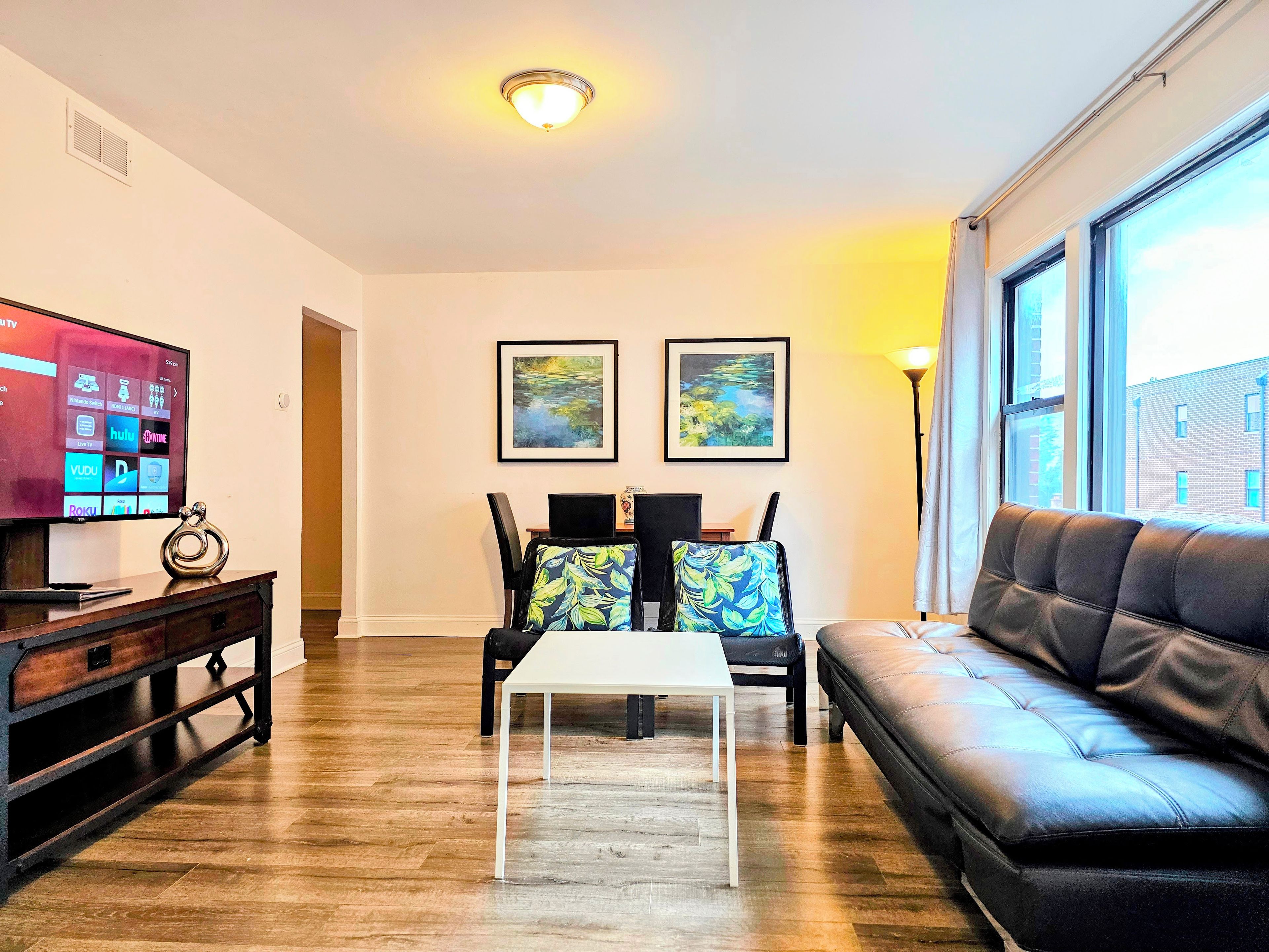 A living room with a flat-screen TV, two framed paintings, a leather sofa, and a wooden coffee table.