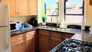 Une cuisine avec des meubles en bois, un four à micro-ondes, une machine à café, un évier et une fenêtre avec des rideaux.
