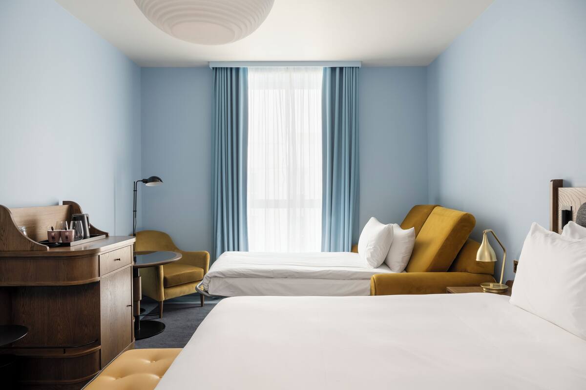 A hotel room with a bed, a desk, a chair, and a lamp.