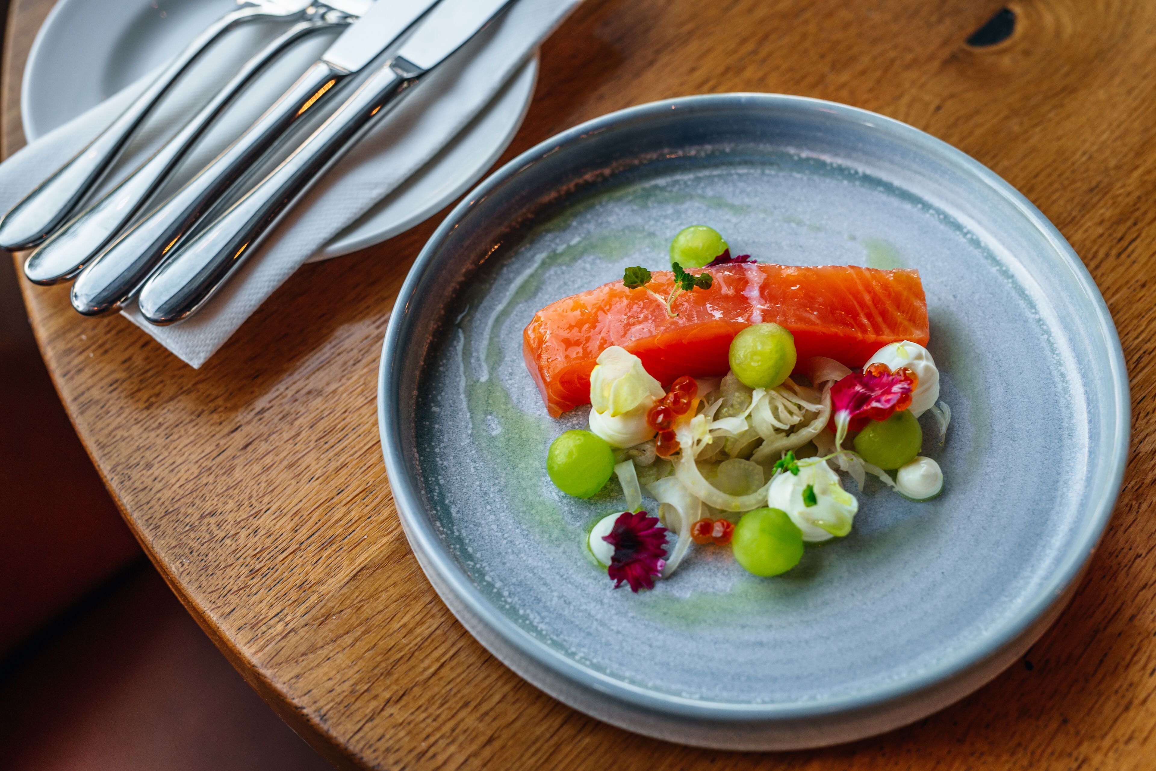 A plate of food with salmon, grapes, and other garnishes on a wooden table.