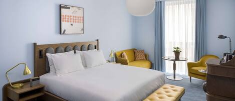 A hotel room with a large bed, a bedside table with a lamp, a small round table with a plant, and a yellow armchair.