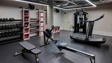 Un gimnasio con equipo de ejercicio, incluyendo mancuernas, una máquina de remo y una cinta de correr.
