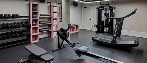 Uma academia com equipamentos de ginástica, incluindo halteres, uma máquina de remo e uma esteira.