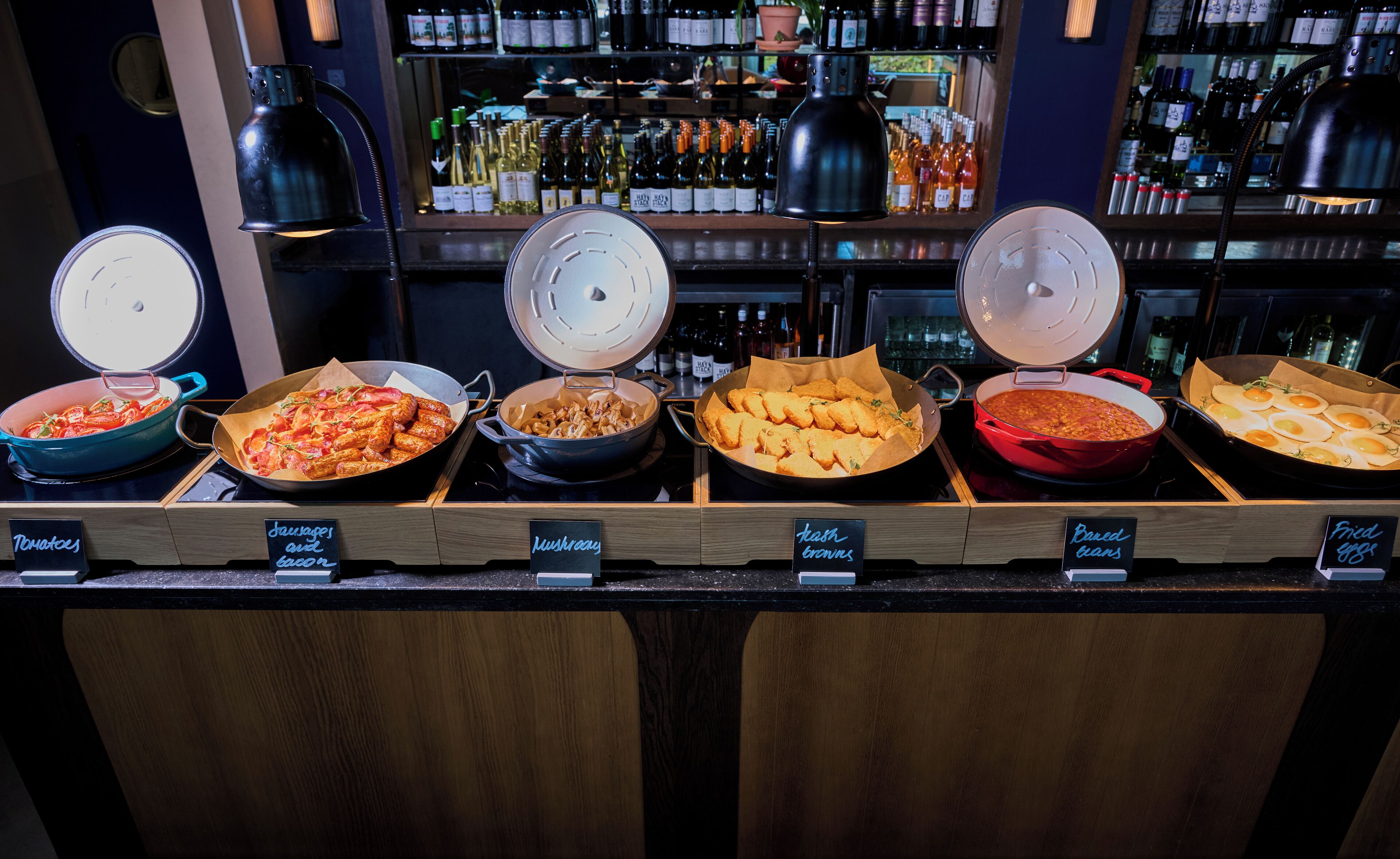 Un buffet proposant divers plats, comme des saucisses, des champignons et des œufs au plat.