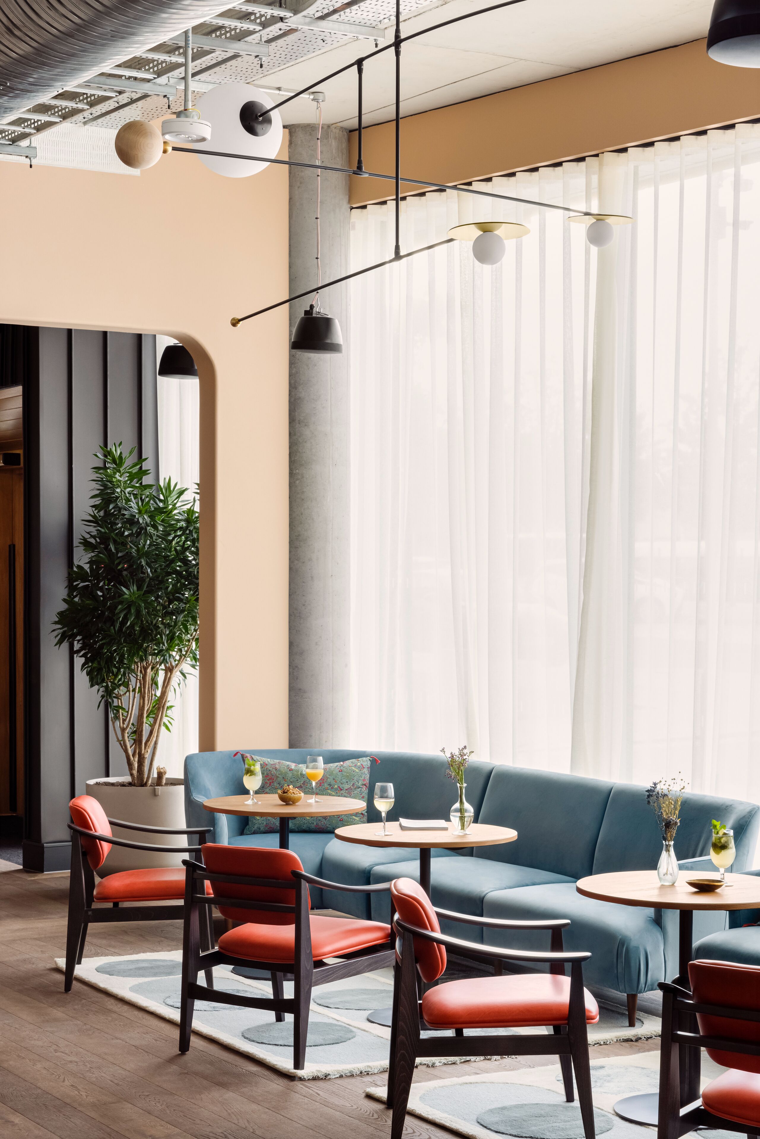 A modern interior with a blue sofa, red chairs, and round tables with drinks.