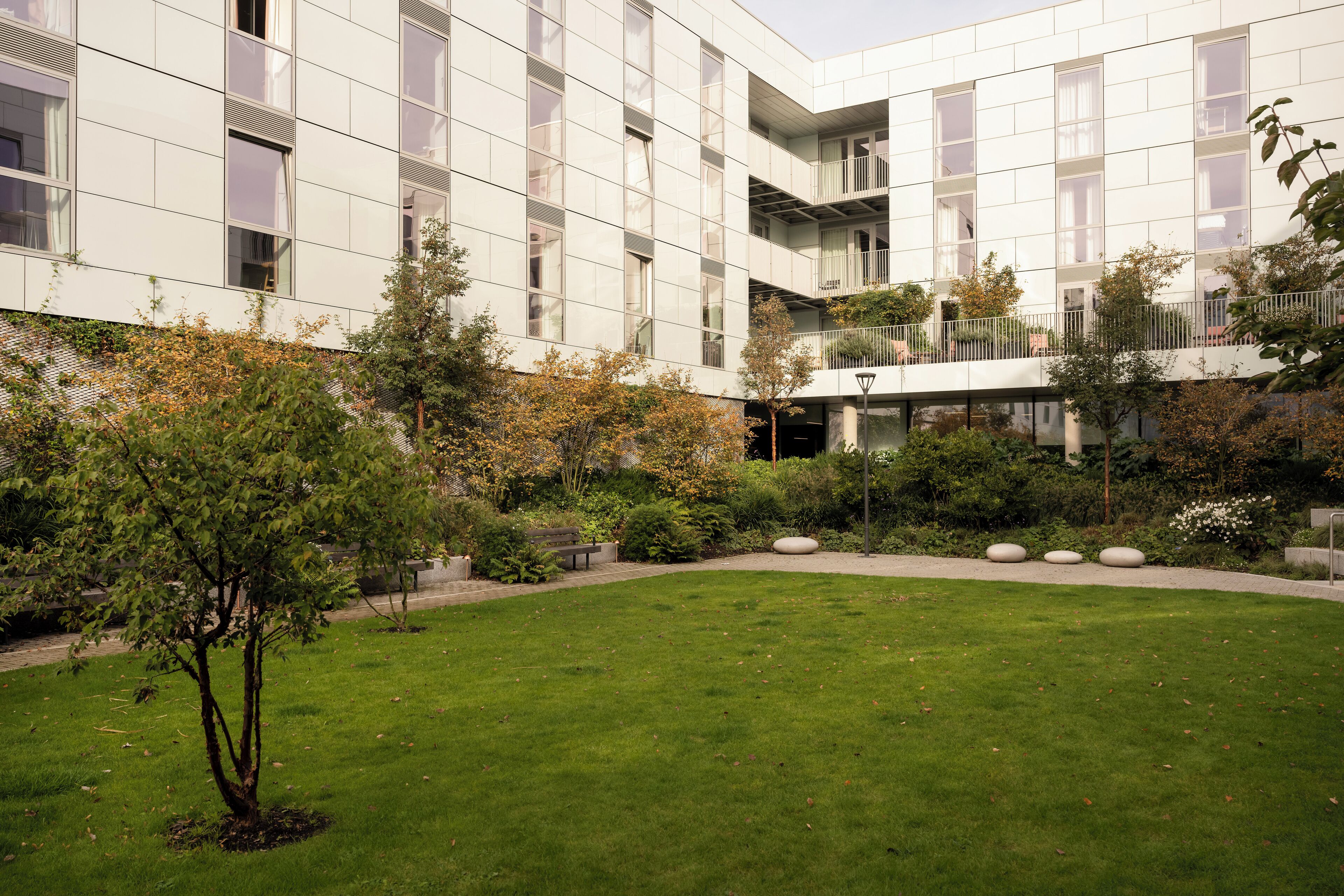 A modern building with a courtyard featuring a lawn, trees, and a bench.