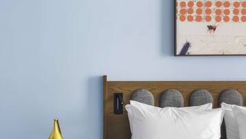 Una habitación de hotel con una cama bien hecha, una mesita de noche con una lámpara, un reloj y una obra de arte en la pared.