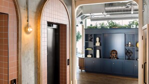Un pasillo con un ascensor moderno, un armario azul con objetos decorativos y vistas al exterior a través de un arco abierto.
