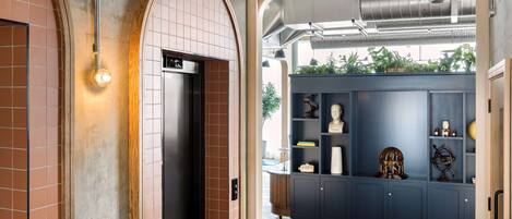 A hallway with a modern elevator, a blue cabinet with decorative items, and a view of the outdoors through an open archway.