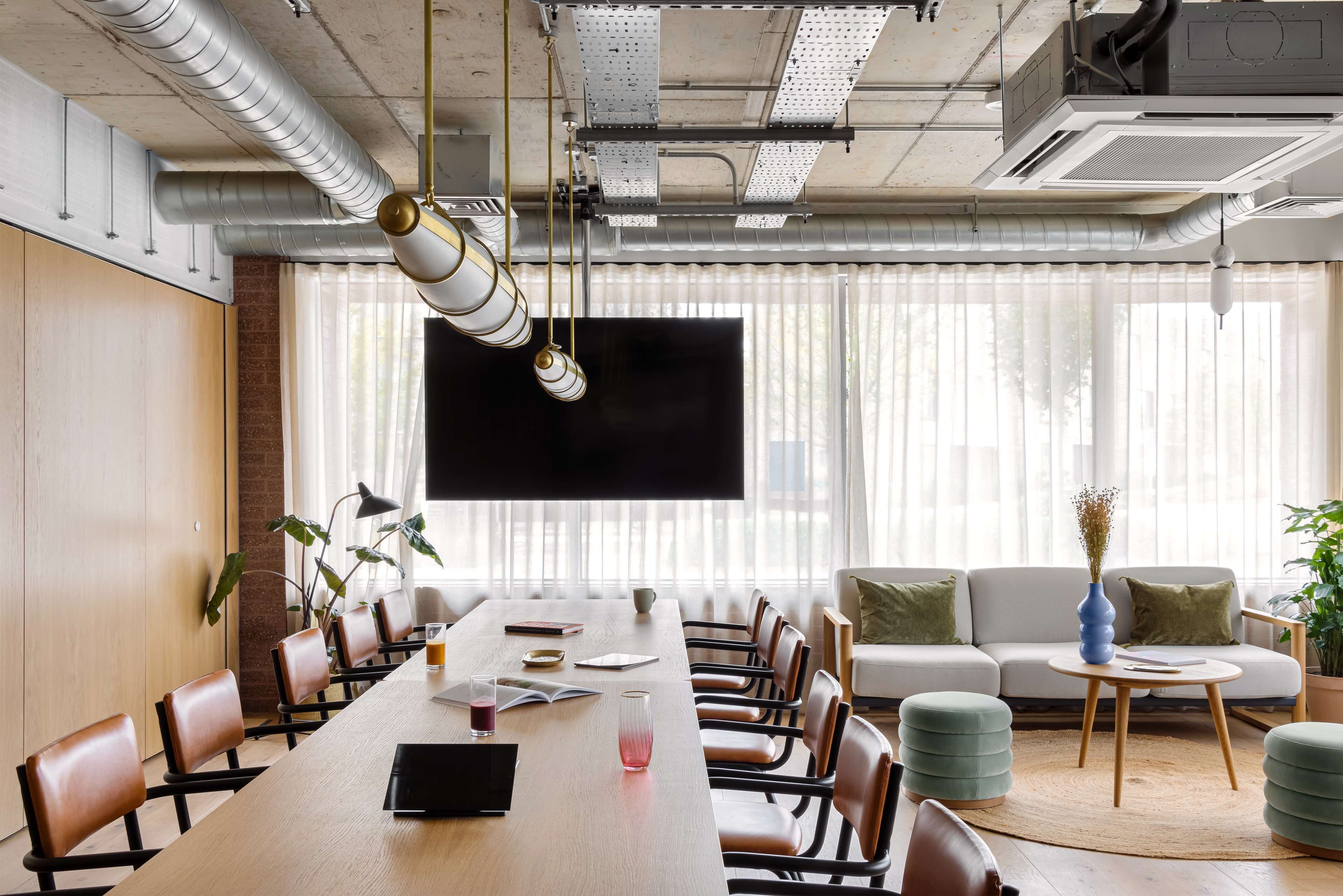 A conference room with a long table, chairs, a sofa, and a TV screen.