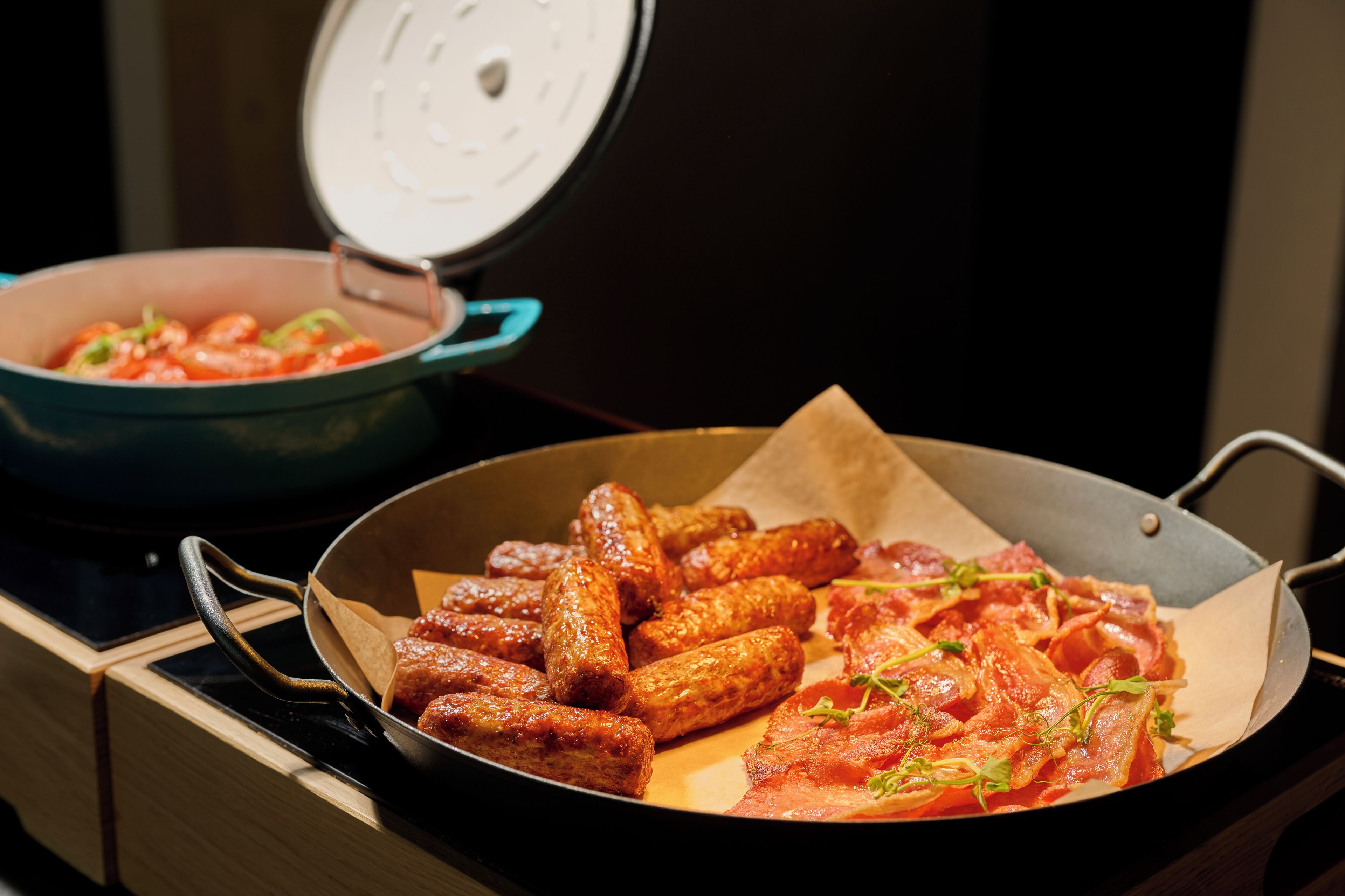 Una cocina con una sartén de salchichas y una olla de tomates.