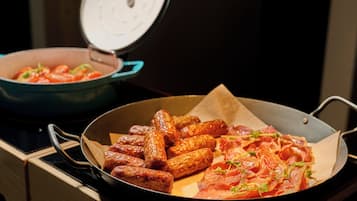Una cocina con una sartén de salchichas y una olla de tomates.