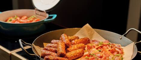 A kitchen with a pan of sausages and a pot of tomatoes.