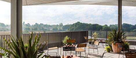 Una zona patio all'aperto con tavoli e sedie, piante in vaso e vista sul paesaggio.