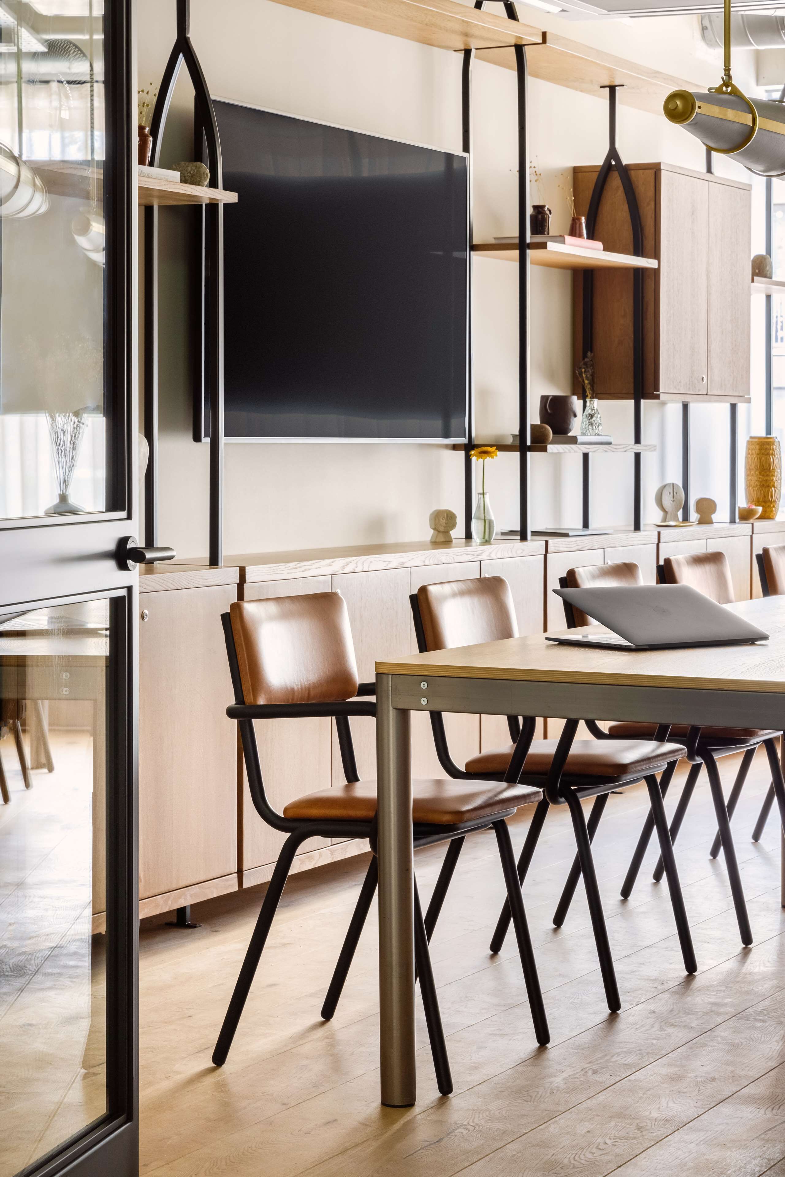 A modern dining area with a long table, multiple chairs, and a large flat-screen TV mounted on the wall.