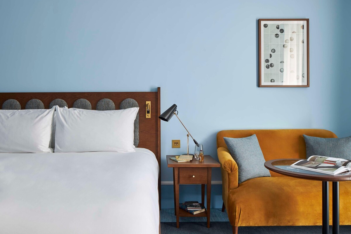 A hotel room with a bed, a nightstand, a table, and a sofa.