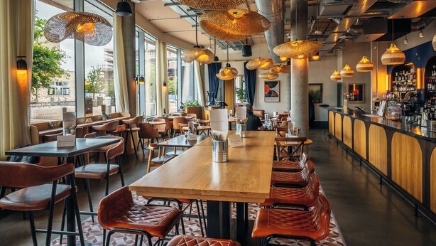 Interior moderno de restaurante con techos altos, conductos expuestos y una larga barra de madera.