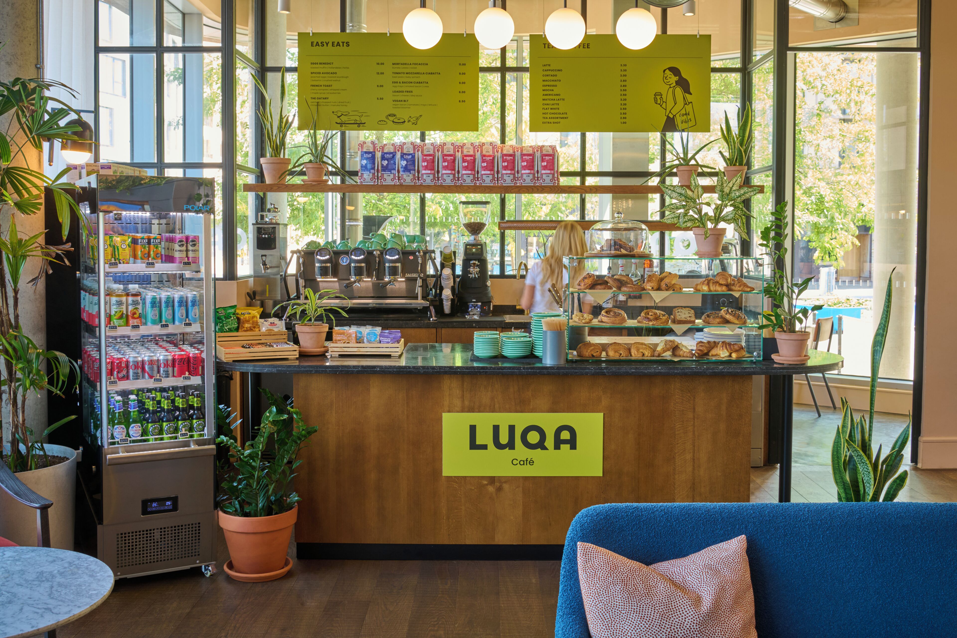 A café interior with a wooden counter, menu boards, a coffee machine, and a variety of pastries.