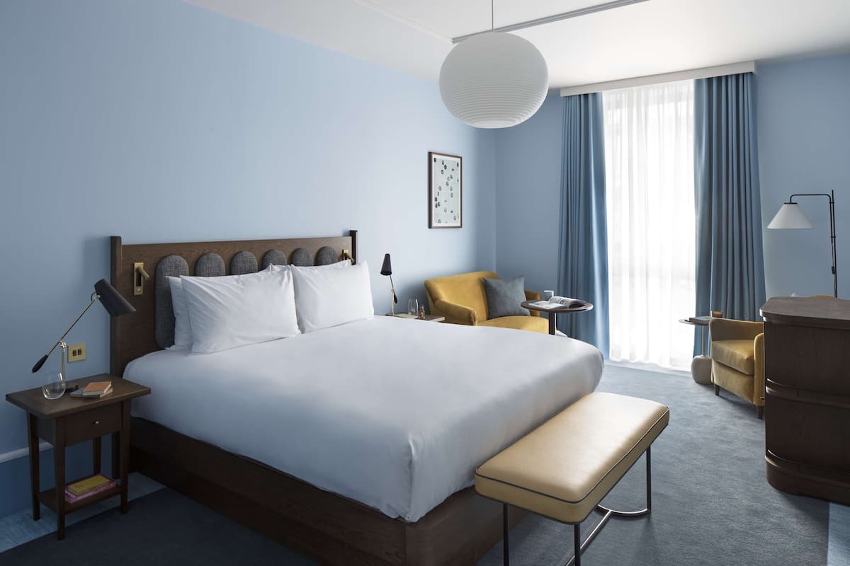 A hotel room with a large bed, bedside tables, a bench, a desk, a chair, and a lamp.