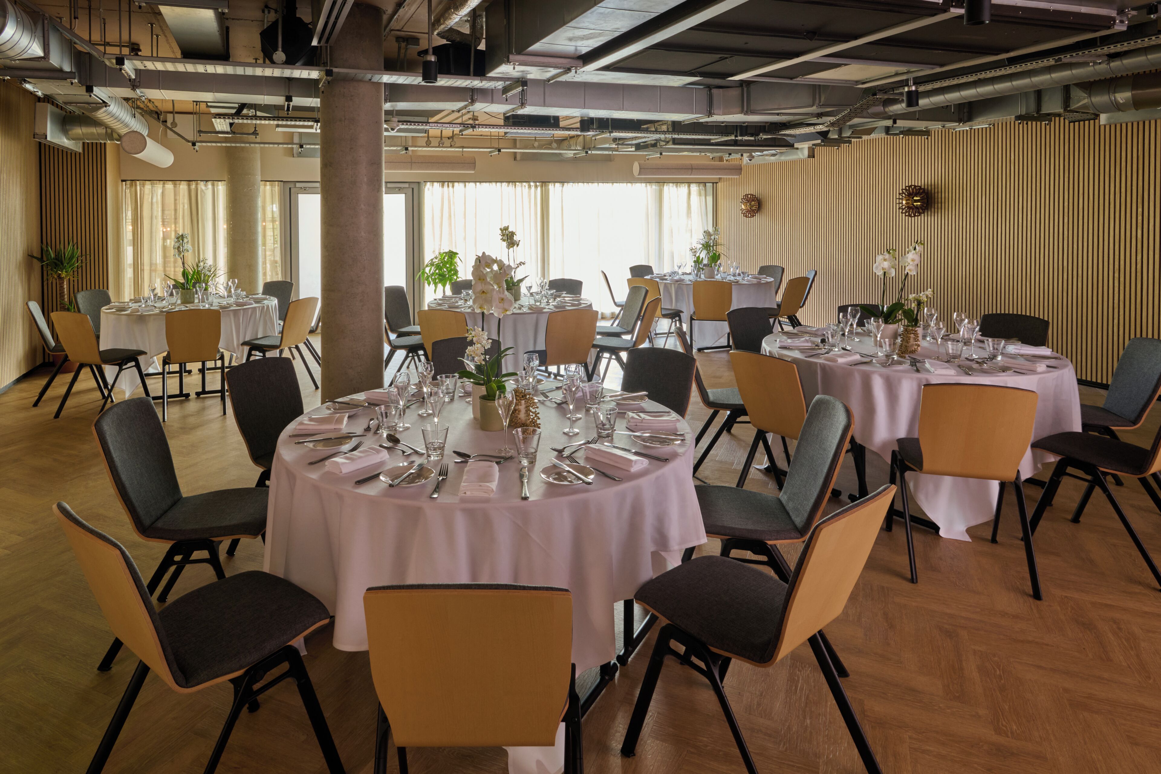 A spacious dining area with round tables set for a meal, surrounded by chairs.