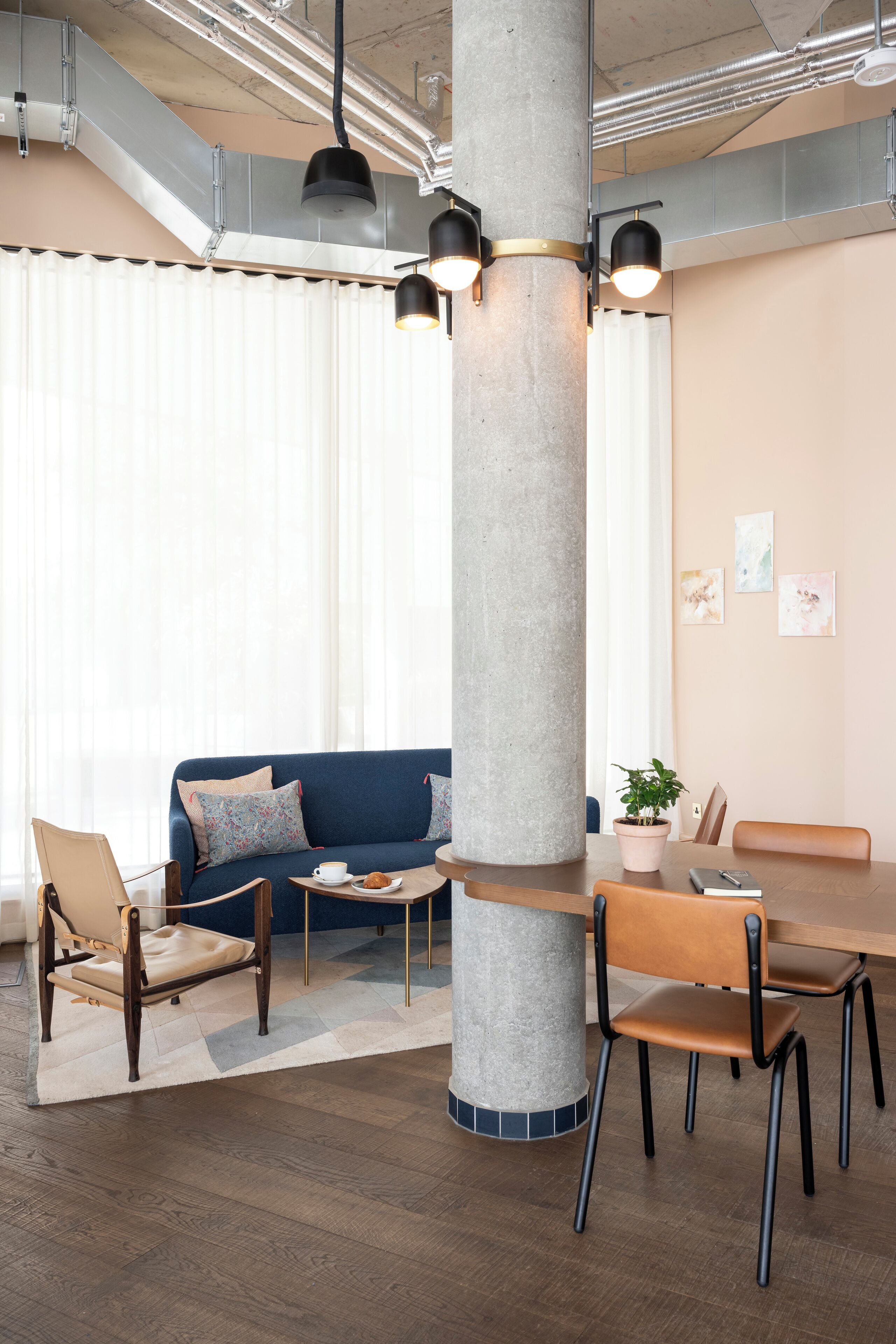 A modern conference room with a large central pillar, a blue sofa, wooden chairs, and a table with a potted plant.