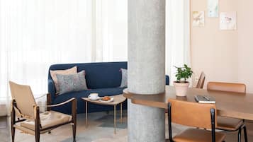 A modern conference room with a large central pillar, a blue sofa, wooden chairs, and a table with a potted plant.