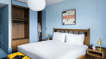 A bedroom with a bed, bedside table, lamp, and a hanging coat rack.