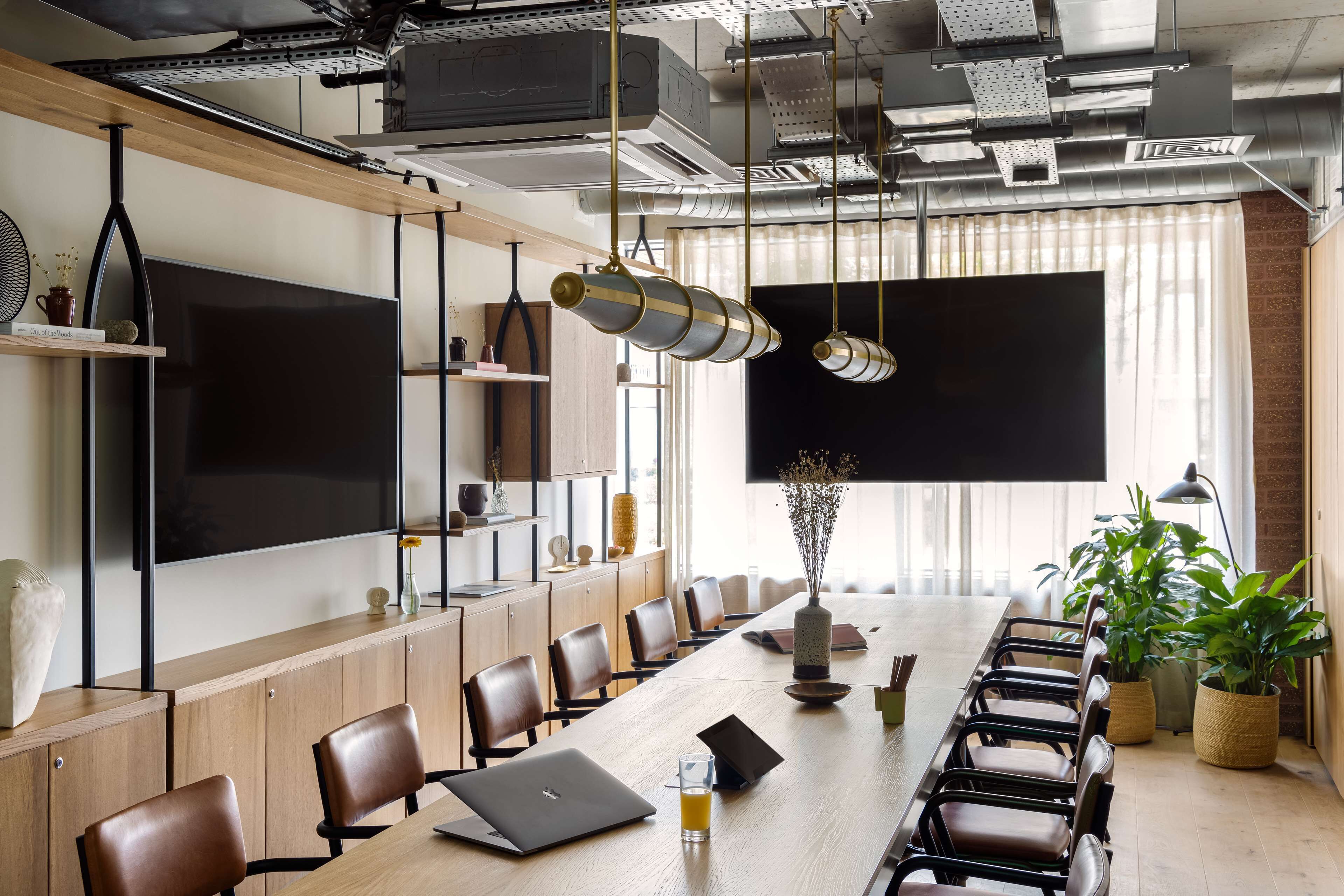 A conference room with a long table, chairs, a large screen, and hanging pendant lights.