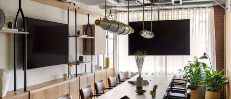 A conference room with a long table, chairs, a large screen, and hanging pendant lights.