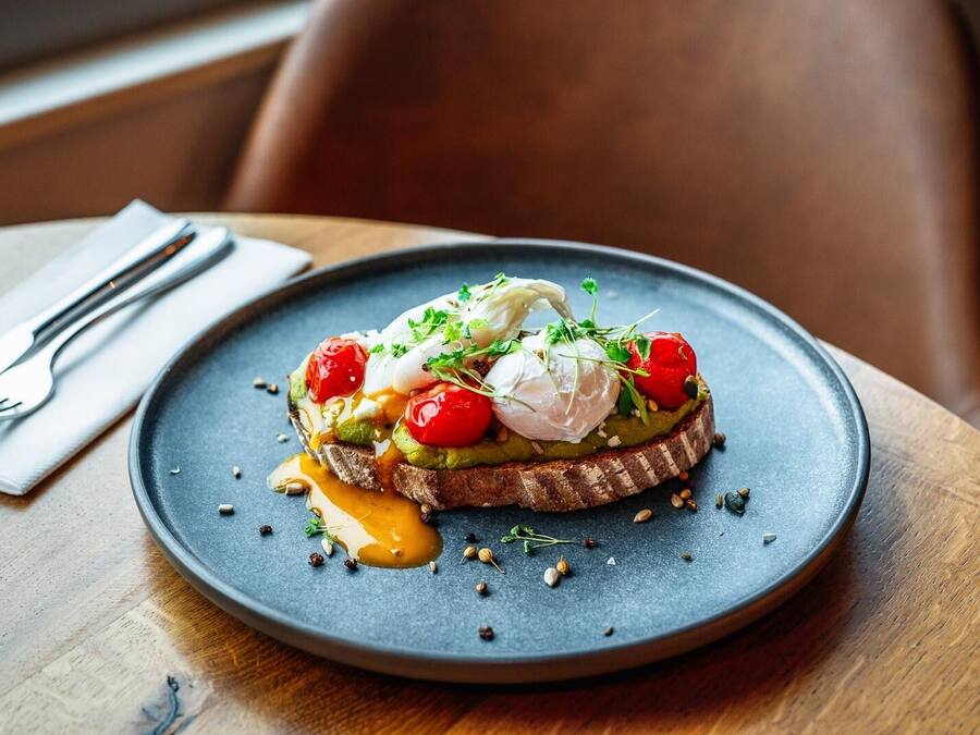 A plate with a dish consisting of avocado, cherry tomatoes, and a poached egg on a slice of bread, garnished with herbs.