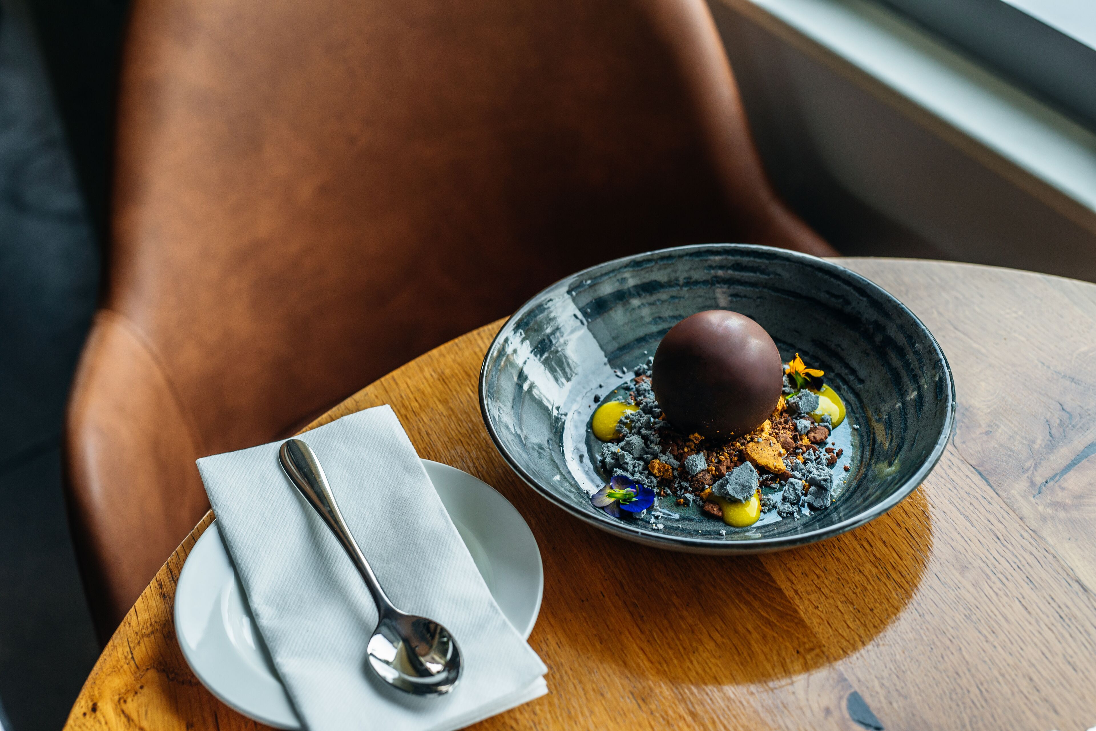 Un dessert servi sur une assiette en céramique, accompagné d’une cuillère et d’une serviette, le tout posé sur une table en bois.