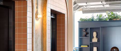 Un vestíbulo moderno con un ascensor de estructura de madera, una estantería azul con adornos y una pared de concreto con diseño de baldosas.