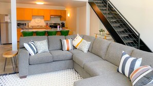 Un saló modern amb un sofà seccional gris, una petita taula auxiliar de fusta i una escala que condueix a un nivell superior.