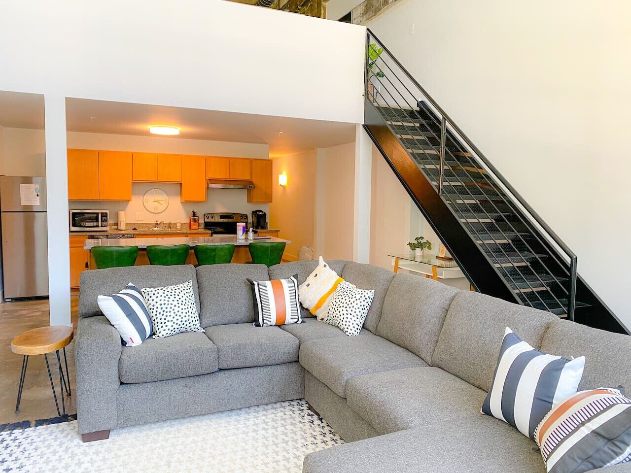 A modern living room with a grey sectional sofa, a small wooden side table, and a staircase leading to an upper level. - The coolest loft in Cincinnati Area (Maineville)